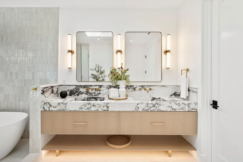 Modern double vanity bathroom with marble countertops and gold fixtures.